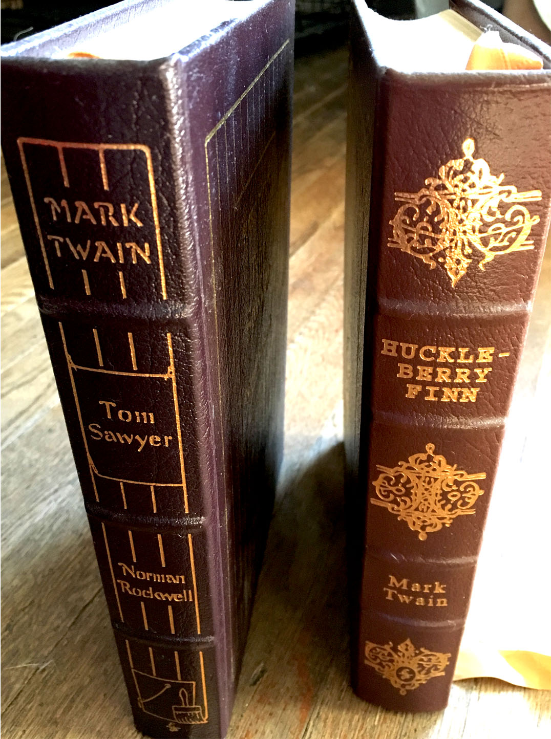 The Adventures of Tom Sawyer and The Adventure of Huckleberry Finn books standing on a floor, leather cover, classic novels.